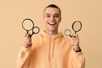 Young man with magnifiers on beige background