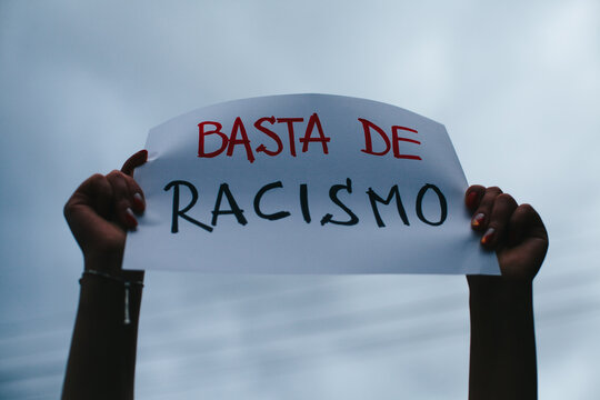 photograph of hands holding a sign with the phrase "no to racism" in Spanish.