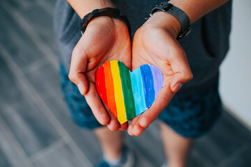 Photograph of man's hands holding a hand drawn LGBTQ+ heart. Concept of people and lifestyles.
