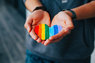 Photograph of man's hands holding a hand drawn LGBTQ+ heart. Concept of people and lifestyles.