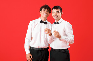 Married gay couple with glasses of champagne on red background