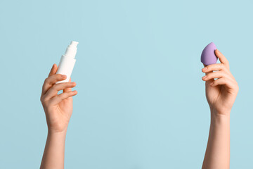 Female hands with makeup sponge and bottle of foundation on blue background