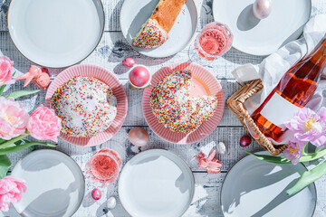 Easter holidays table, pink wine in glasses, Easter cakes, color eggs, served plates, flowers tulips on white background for festive dinner at home. Holiday concept, top view, flat lay