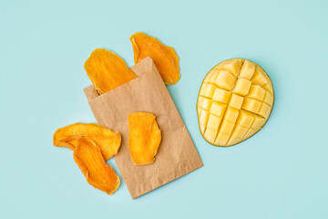 Paper bag with slices of dried mango on blue background