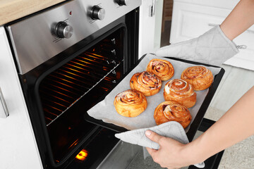 Woman taking baking tray with buns from oven in kitchen, closeup