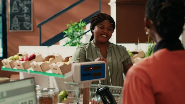 Local vendor counting and scanning goods for customer at bio natural supermarket, african american woman encourages nutritious food. Shopper on the lookout for non toxic produce at store.