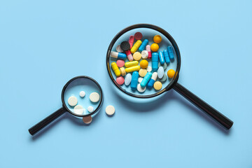 Magnifying glasses with different pills on blue background