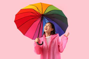 Beautiful young Asian woman in raincoat with umbrella on pink background
