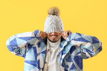 Young man in winter clothes on yellow background