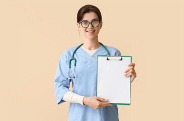 Female medical intern with clipboard on beige background