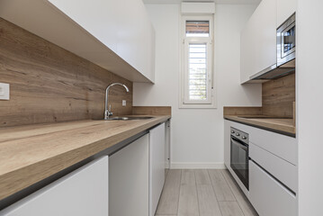 A small kitchen with smooth white furniture, wooden countertops that match the backsplashes, light parquet floors
