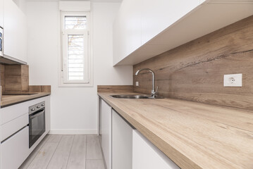A small kitchen with smooth white furniture without handles and wooden countertops that match the backsplashes