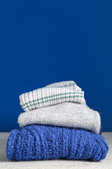 Stack of different stylish sweaters on color background