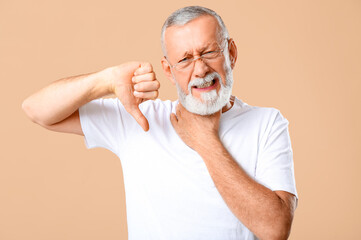 Ill old man with sore throat showing thumb-down on beige background