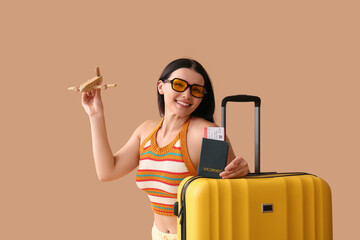 Happy young woman with wooden plane, passport and suitcase on color background