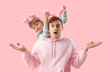 Little boy with his shocked father in bunny ears on pink background. Easter celebration