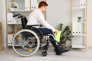 Young businessman in wheelchair watering plant at office