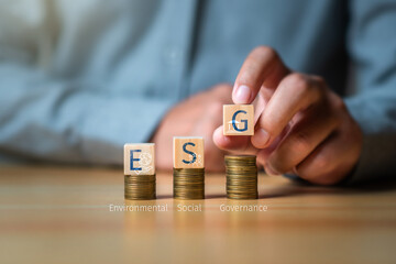 ESG sustainable investment concept, investor put a wooden cubic with text ESG on coinstack ,...