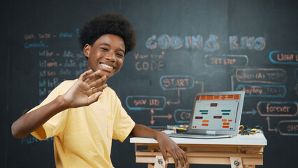 Smart african boy use laptop to code program and turn around to wave hand. Cute highschool stident coding engineering prompt or program system at blackboard in STEM technology classroom. Edification - obrazy, fototapety, plakaty