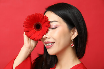 Happy young Asian woman with beautiful gerbera flower on red background