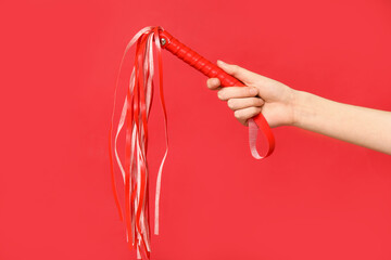 Female hand with whip from sex shop on red background