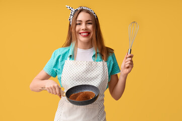 Happy young woman holding frying pan with tasty pancakes and whisk on yellow background