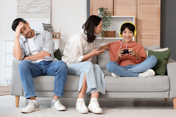 Teenage boy playing video game and his upset parents at home. Family problem concept © Pixel-Shot