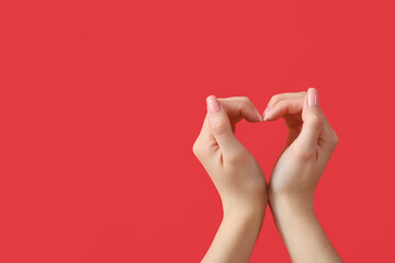 Female hands showing heart gesture on red background. Valentine's Day celebration