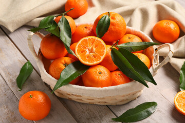 Wicker basket with sweet mandarins and leaves on grey wooden background