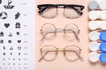 Stylish eyeglasses with eye test chart and containers for contact lenses on beige background