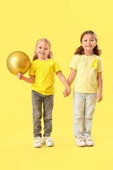 Fototapeta premium Cute little girls with yellow ribbons and air balloon on color background. Childhood cancer awareness concept
