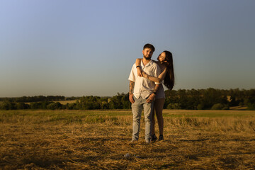 Beautiful couple hugging and kissing in a field at sunset