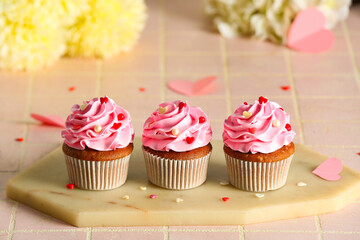 Board with tasty cupcakes for Valentine's Day on pink tile background