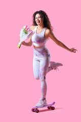 Young African-American woman in sportswear with bouquet of tulips riding skateboard on pink...
