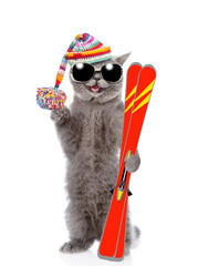 Happy cat wearing sunglasses and warm woolen hat with pompom holds skis in it paw. Isolated on white background
