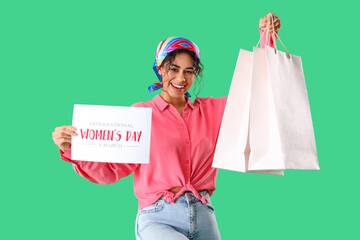 Fashionable African-American woman holding paper sheet with text INTERNATIONAL WOMEN'S DAY and shopping bags on green background. International Women's Day celebration