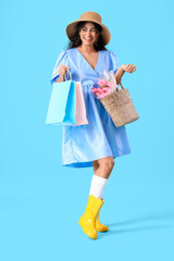 Fashionable African-American woman with bouquet of flowers and shopping bags on blue background. International Women's Day celebration