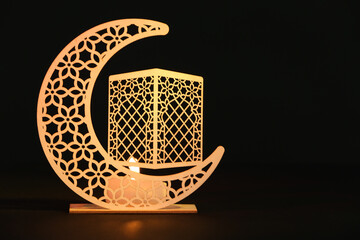 Decorative crescent with burning candle for Ramadan on table against dark background