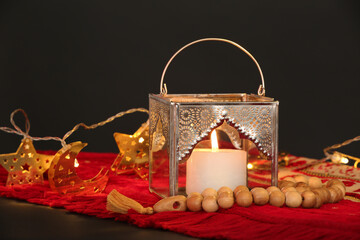 Red mat with silver Muslim lamp and prayer beads for Ramadan on dark background