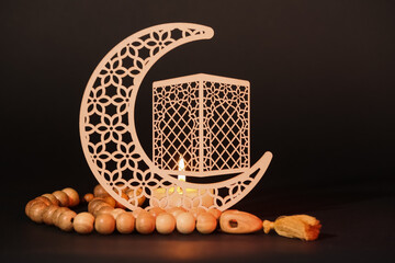 Decorative crescent with burning candle and prayer beads for Ramadan on table against dark...