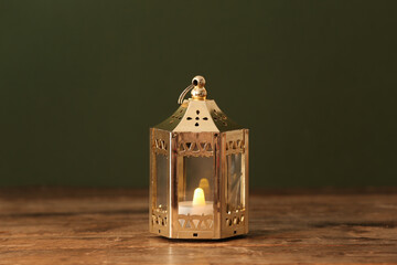 Silver Muslim lamp with burning candle for Ramadan on wooden table against dark green background