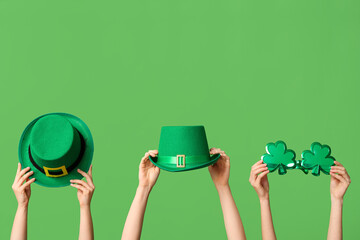 Female hands holding leprechaun's hats and novelty glasses on green background. St. Patrick's Day...