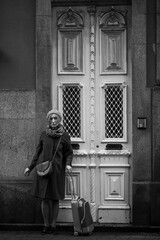 A woman with a suitcase knocks on the door of a traditional house in Porto, Portugal. Black and white photo.