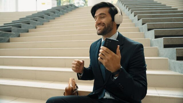 Happy smart business man taking selfie while smiling at smart phone. Closeup image of professional executive manager sitting at stairs while wearing suit and headphone. Creative business. Exultant.