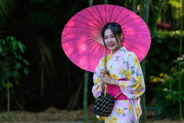 A young woman wearing a Japanese traditional kimono or yukata holding an umbrella is happy and...