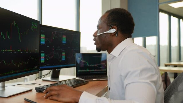 Concentrated african crypto trader sitting in front of computers, making professional analysis of candlestick chart, creating strategy