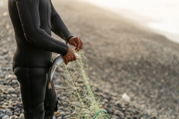 Fisherman in wetsuit unhooking a caught fish from the net
