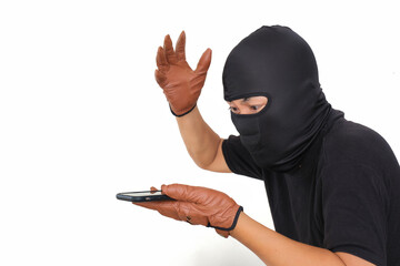 Side view: A man wearing a black t-shirt and balaclava is looking at a smartphone while raising his hand - obrazy, fototapety, plakaty
