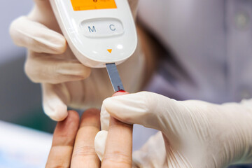 Medical professionals conducting scientific research using blood glucose meters technology in a healthcare laboratory, with a focus on a doctor's hands manipulating the equipment and patient hand. 