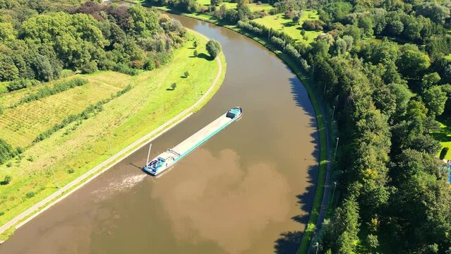 This drone footage presents a bird's-eye perspective of a large cargo ship making its way through a picturesque rural river. The lush greenery of the riverbanks contrasts beautifully with the tranquil